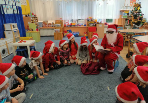 Dzieci siedzą na dywanie, słuchają Mikołaja, który czyta wierszyki o tematyce świątecznej z książki pt. „Choinkowe wierszyki”.